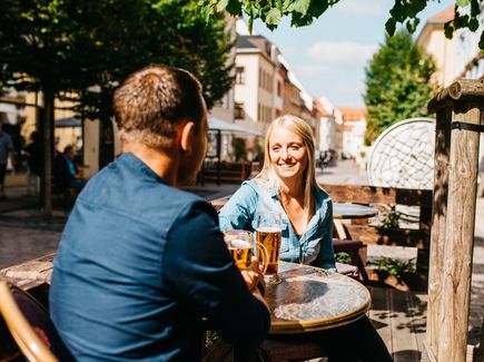 Pärchen sitzt am Tisch und stößt an mit einem Bier