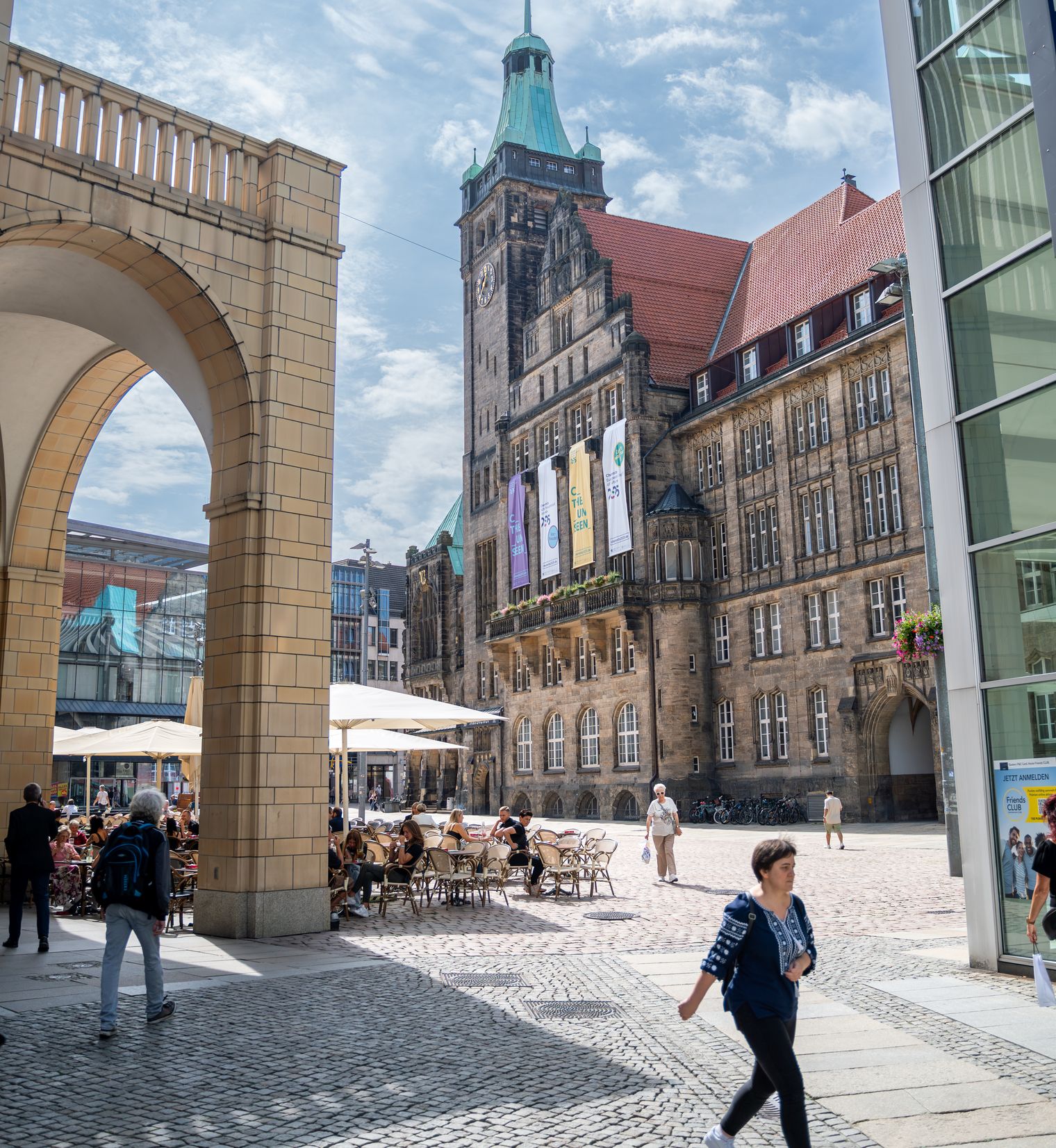 Marktplatz einer größeren Innenstadt gesäumt von historischen und modernen Gebäuden. Ein Mensch läuft uns den gepflasterten Bodenbelag.