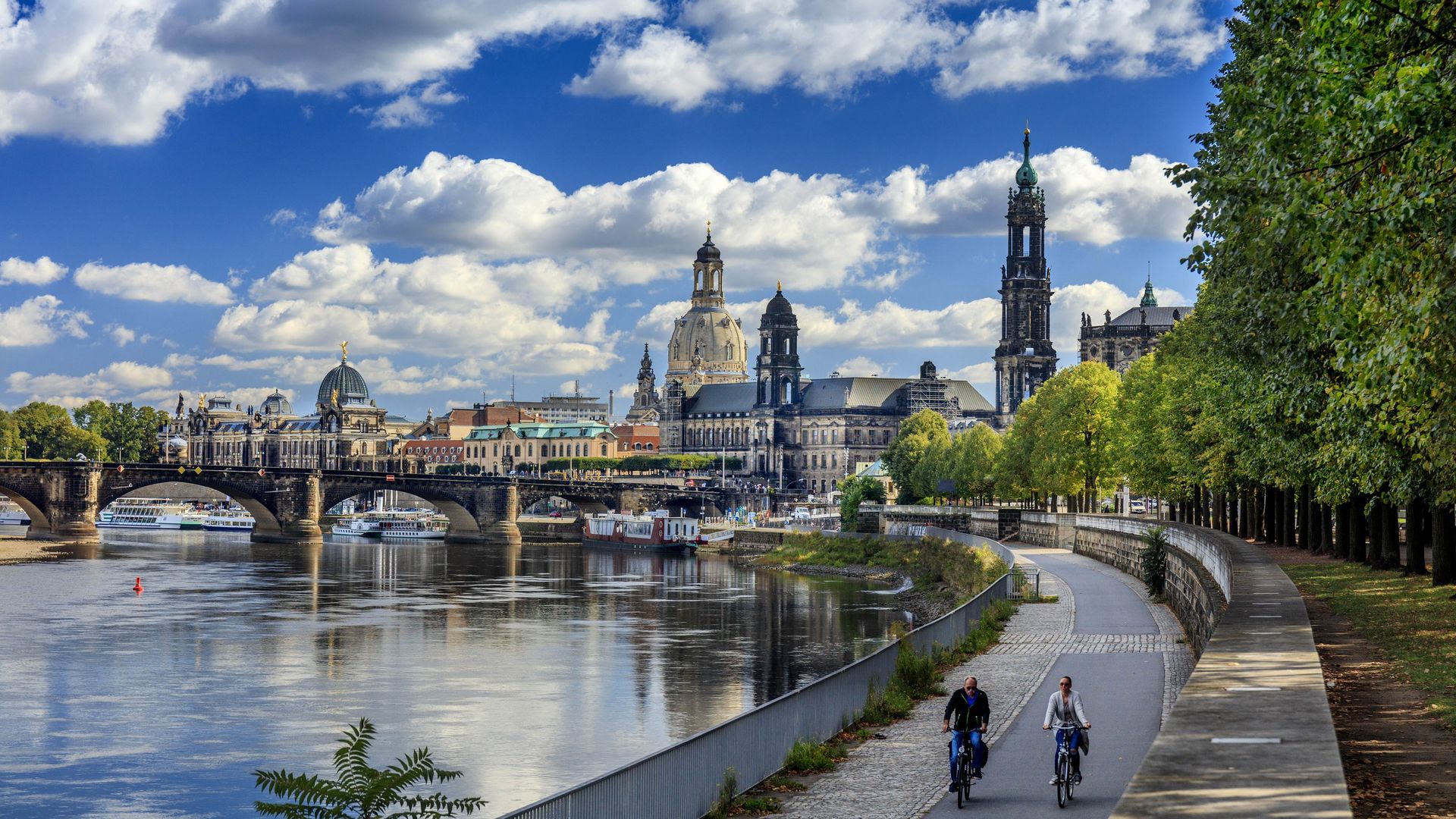 Zwei Radfahrer fahren auf dem Elberadweg entlang . Im Hintergrund sieht man die Altstadt von Dresden.