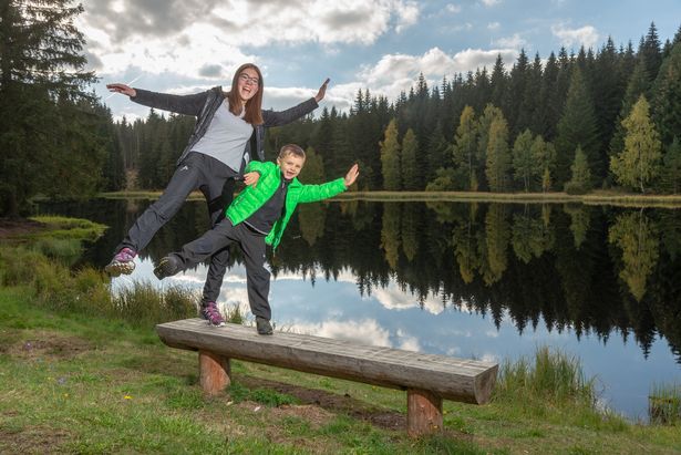 Ein Junge und eine Frau stehen auf einer Bank an einem See bei Morgenröthe-Rautenkranz. 