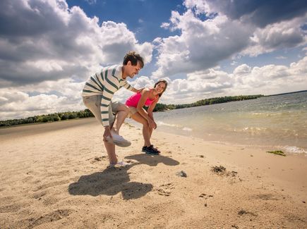 Ein Mann und eine Frau sind am Strand vom Bärwalder See im Lausitzer Seenland. Sie ziehen sich gerade die Schuhe aus.