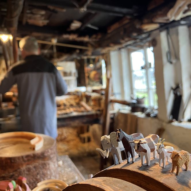 Handwerker in einer traditionellen Holzwerkstatt in Seiffen mit geschnitzten Holzfiguren./ Craftsperson in a traditional wood workshop in Seiffen with carved wooden figures.