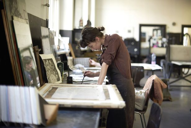 Eine Frau steht an einem Tisch in der Hochschule für Grafik und Buchkunst Leipzig. Sie arbeitet an einem Siebdruck. 