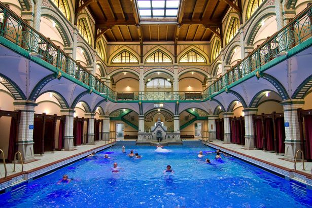 Besucher schwimmen in einem Becken des Johannisbad in Zwickau. Die Wände sind verziert und ein prunkvolles Geländer umrahmt das Ganze. 