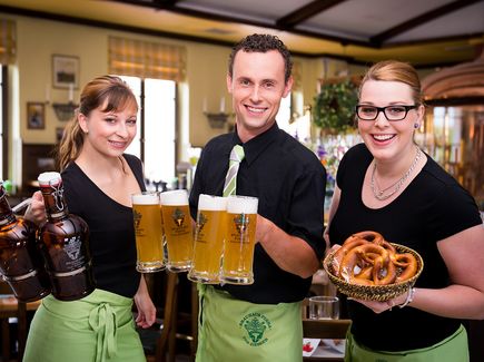 Drei Servicekräfte präsentieren Bier und Brezeln