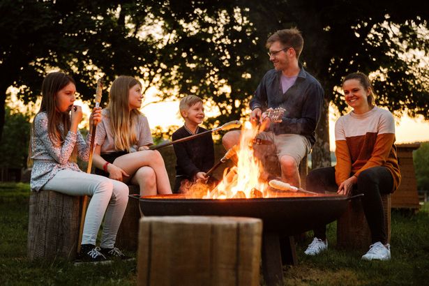 Familie sitzt mit Stockbrot am Lagerfeuer und unterhält sich über die Erlebnisse des zurückliegenden Tages.