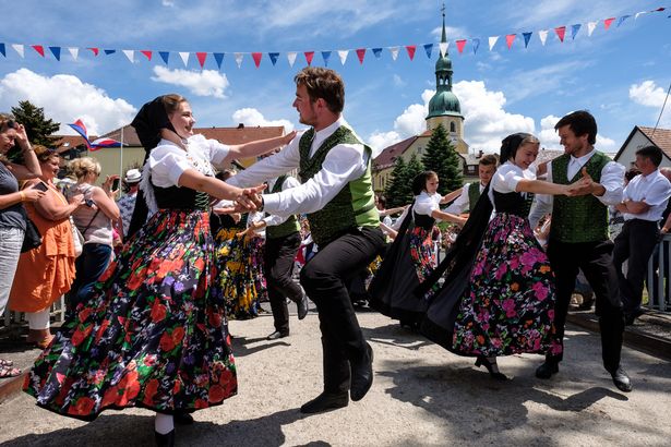 Mehrere Pärchen in sorbischer Tracht tanzen bei einem internationalen Folklorefestival. Am Rand stehen Zuschauer und Zuschauerinnen und bestaunen das Spektakel.