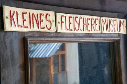 Ein Holzschild, auf dem mit roter Schrift steht "Kleines Fleischereimuseum". 
