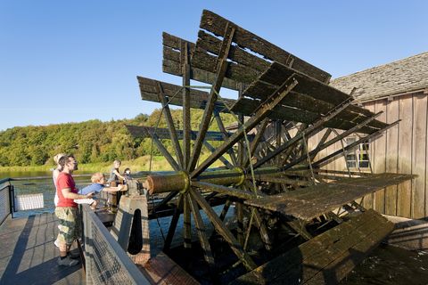 Eine Familie steht an einem Mühlrad. Sie sind an der Technischen Schauanlage der Schiffmühle bei Höfgen. 