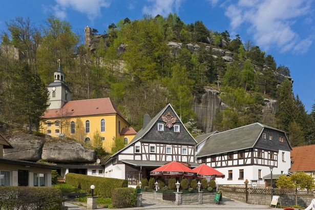 Hinter Fachwerkhäusern und einer Kirche erhebt sich der Berg von Oybin. 