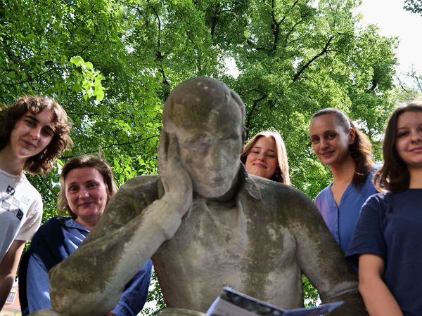 Junge Menschen stehen neben der Statue einer lesenden Person