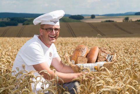 Ein Bäcker hat einen Brotkorb in der Hand und sitzt in einem Getreidefeld bei Höckendorf. 