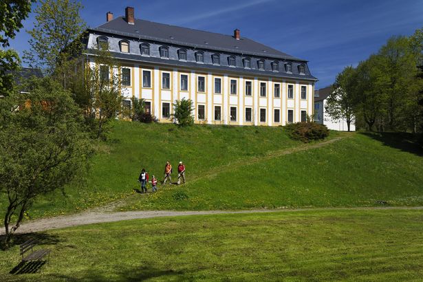 Spaziergänger laufen von einer Anhöhe herunter. Auf ihr steht das Schloss Leubnitz. 