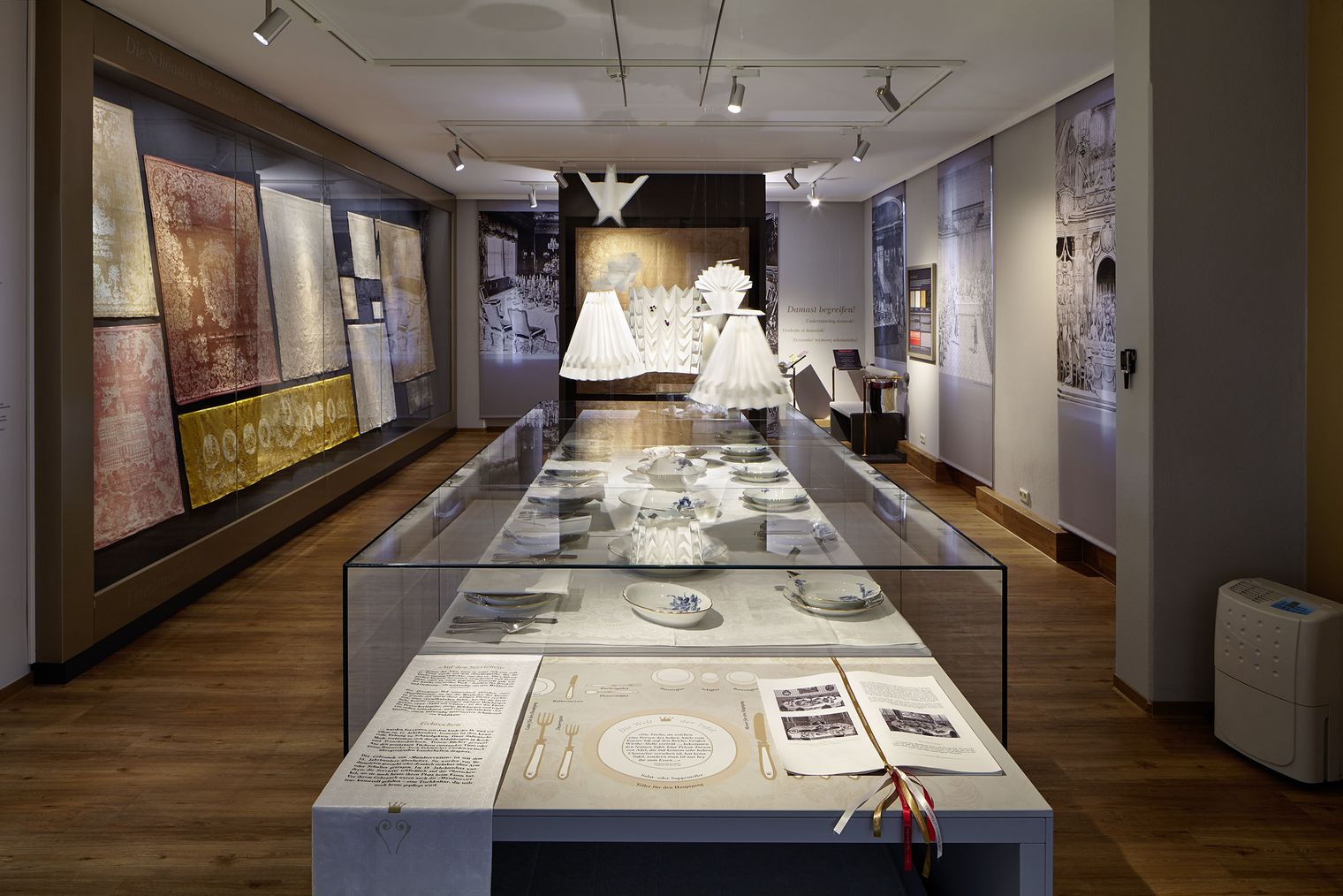 Ausstellungsraum des Damast- und Frottiermuseums mit historischen Damaststoffen, gedeckter Tafel mit Porzellan und kunstvoll gefalteten Textilien.