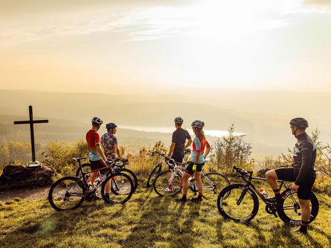 Fünf Radfahrer stehen an einer Aussichtshöhe mit Gipfelkreuz. Sie sind auf der Stoneman-Road.