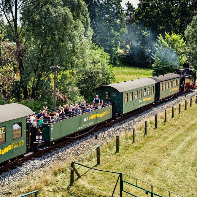 Eine grüne Bahn fährt an einer Wiese vorbei. Es ist die Lößnitzgrundbahn bei Radebeul. 