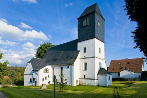 Eine weiß gestrichene Kirche mit einem dunklen Dach steht auf einer Wiese in Höckendorf.
