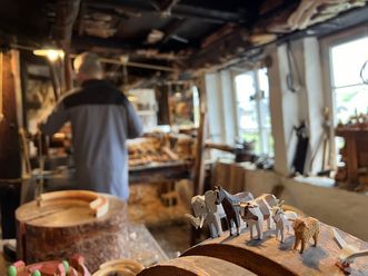 Handwerker in einer traditionellen Holzwerkstatt in Seiffen mit geschnitzten Holzfiguren./ Craftsperson in a traditional wood workshop in Seiffen with carved wooden figures.