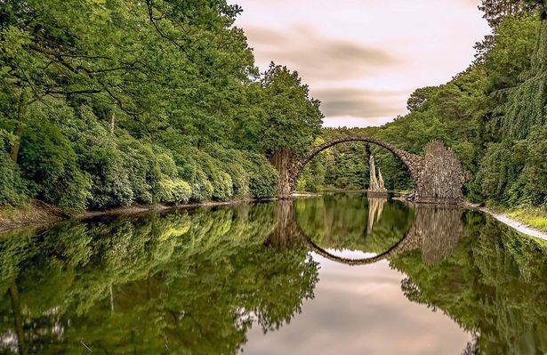 Die Rakotzbrücke spannt sich über einen Teich im Rhododendronpark Kromlau und spiegelt sich im Wasser. 