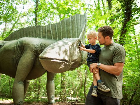 Ein Mann hat seinen Jungen auf dem Arm, der einen Dinosaurier streichelt. Sie sind im Saurierpark in der Oberlausitz.