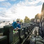 Menschen schauen von der Basteibrücke in der Sächsischen Schweiz herunter in die Landschaft. 