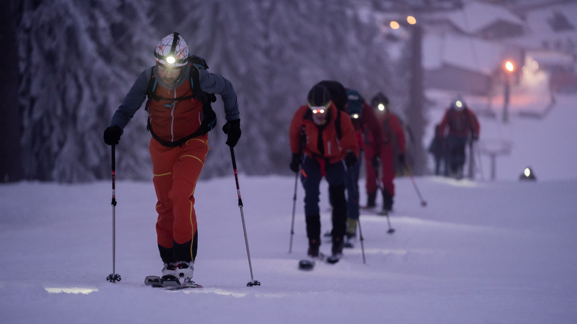 Skitourengänger wandern in der Dunkelheit in einer Reihe einen verschneiten Hang hinauf.