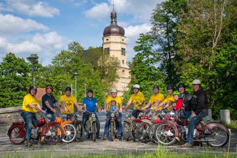 Zehn Männer sitzen auf ihren Mopeds und haben sich zu einem Gruppenbild vor der Kirche von Kürbitz aufgestellt. 