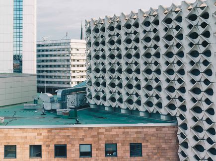 Zu sehen sind mehrere Gebäude hintereinander als Ausschnitt der Stadtansicht von Chemnitz. Im Vordergrund sieht mal ein flaches Gebäude in rötlicher Fassade, auf dem Antennen stehen. 