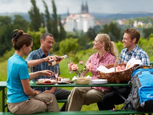 Vier Personen sitzen an einem Tisch mit Sekt und Essen, mit der Albrechtsburg Meißen im Hintergrund 