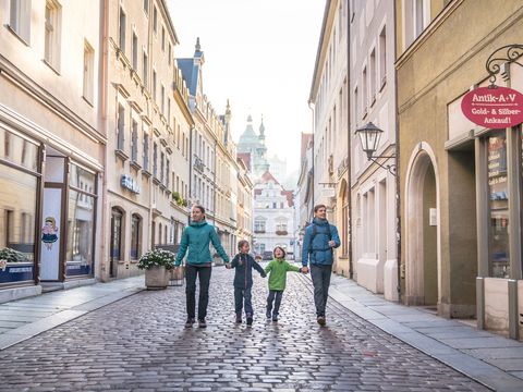 Eine Familie läuft durch die Altstadt von Pirna, vorbei an kleinen Einkaufsläden.