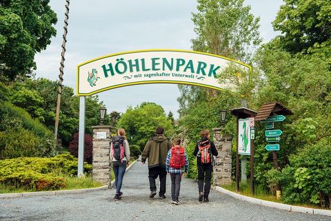 Eine Familie wandert mit Rucksäcken unter einem großen Schild hindurch auf dem "Höhlenpark" steht.