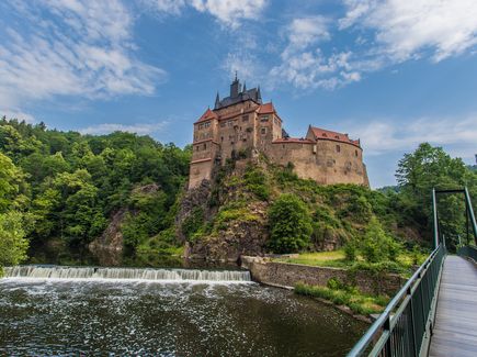 Eine Burg auf einer Anhöhe an der ein Fluss vorbei fließt. 