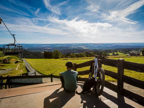 Biker neben seinem Bike an Mountainbikestrecke bei strahlend blauem Himmel