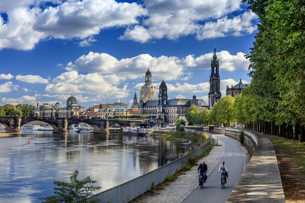 Zwei Radfahrer fahren auf dem Elberadweg entlang . Im Hintergrund sieht man die Altstadt von Dresden.