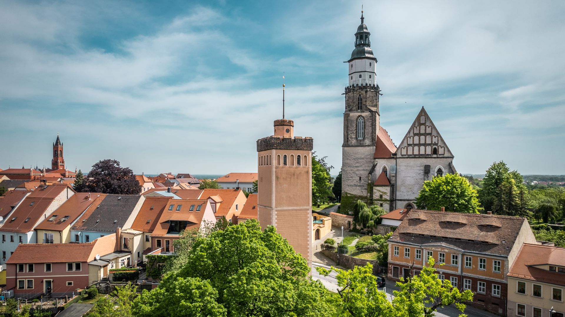 St. Marienkirche mit hohem Turm und Roter Turm mit quadratischem Grundriss in Kamenz, umgeben von roten Dächern und grüner Landschaft / St. Marienkirche with tall tower and Roter Turm with square base in Kamenz, surrounded by red roofs and green landscape