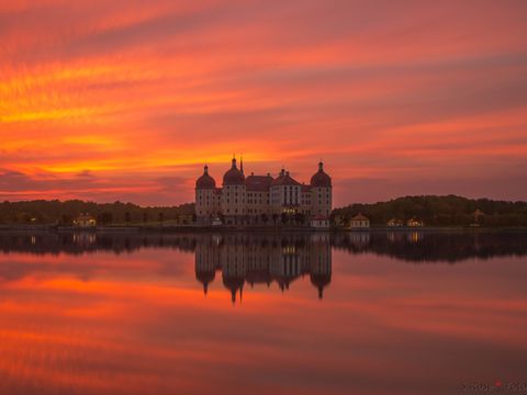 In rotes Licht vom Sonnenuntergang getauchtes Jagdschloss Moritzburg mit seinem Seem 
