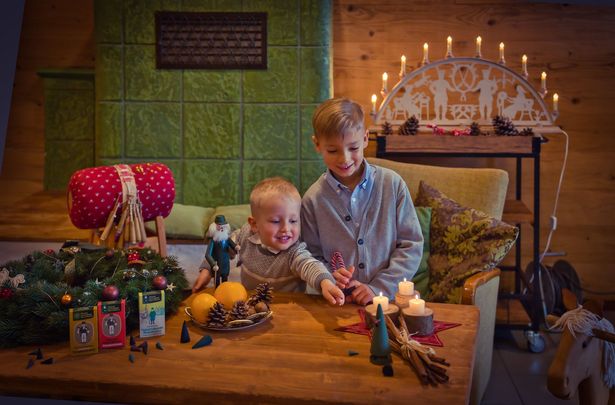 Zwei Kinder sitzen an einem Tisch der weihnachtlich dekoriert wurde und auf dem Räucherkerzen stehen.