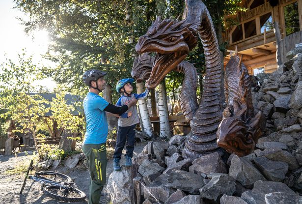 Ein Vater steht mit seinem Sohn vor einem aus Holz gesägten Drachen.
