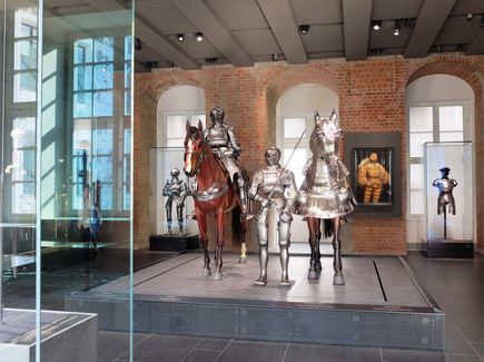 Im Renaissanceflügel des Schlosses in Dresden sind verschiedene Ritterrüstungen ausgestellt. In der Mitte des Raumes sind ebenfalls zwei Pferdefiguren und auf der einen sitzt ein Ritter mit seiner Rüstung und ein anderer Ritter steht neben seinem Pferd.