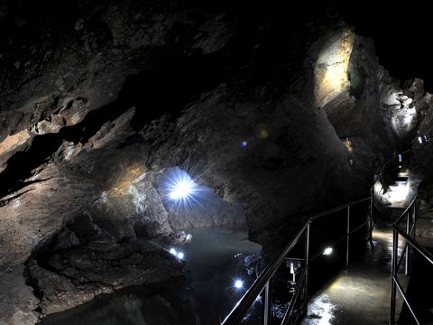 Eine Brücke in der Tiefe der Drachenhöhle Syrau führt über das Wasser. Es ist dunkel, nur einzelne Lichtpunkte leuchten.