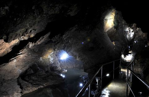 Eine Brücke in der Tiefe der Drachenhöhle Syrau führt über das Wasser. Es ist dunkel, nur einzelne Lichtpunkte leuchten.