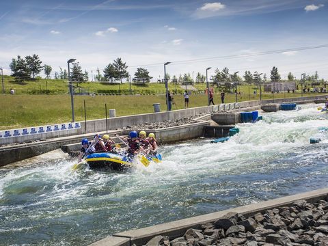 Menschen sitzen in Schlauchbooten und machen Wildwasserrafting auf einem Wasserstrom. Er ist abgegrenzt durch eine Mauer.