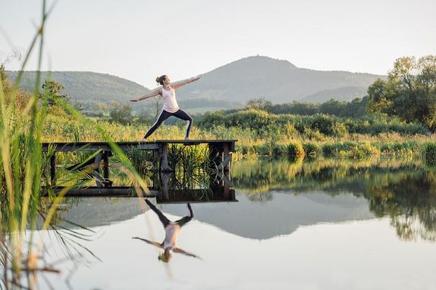 Eine Frau steht in der Yoga-Position Kriegerin auf einem Steg eines Sees. Im Hintergrund ist die Landschaft der Oberlausitz zu sehen.