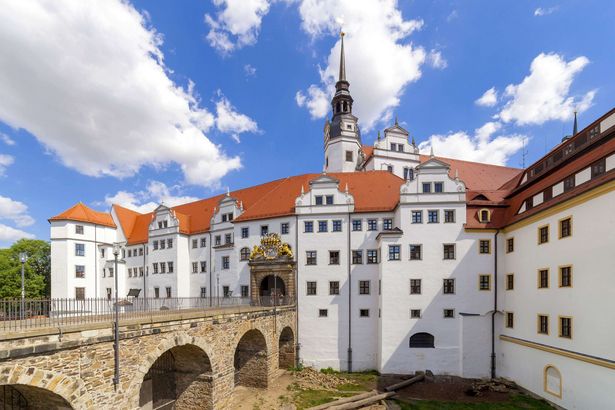 Eine Brücke aus Stein führt zum weißen Schloss Hartenfels.