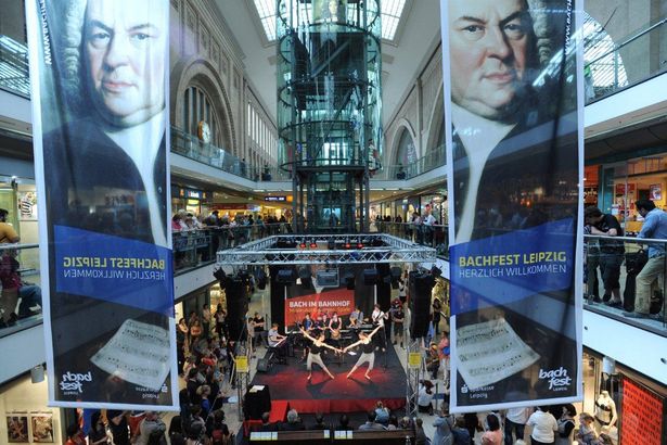 Zuschauer stehen in den Promenaden des Leipziger Hauptbahnhofs. Gerade treten Tänzer beim Bachfest auf und Plakate hängen von den Wänden herunter. 