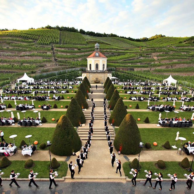Besucher sitzen auf dem Anwesen Schloss Wackerbarth und werden von den Kellnern bedient. Es ist Sommernachtsball. 