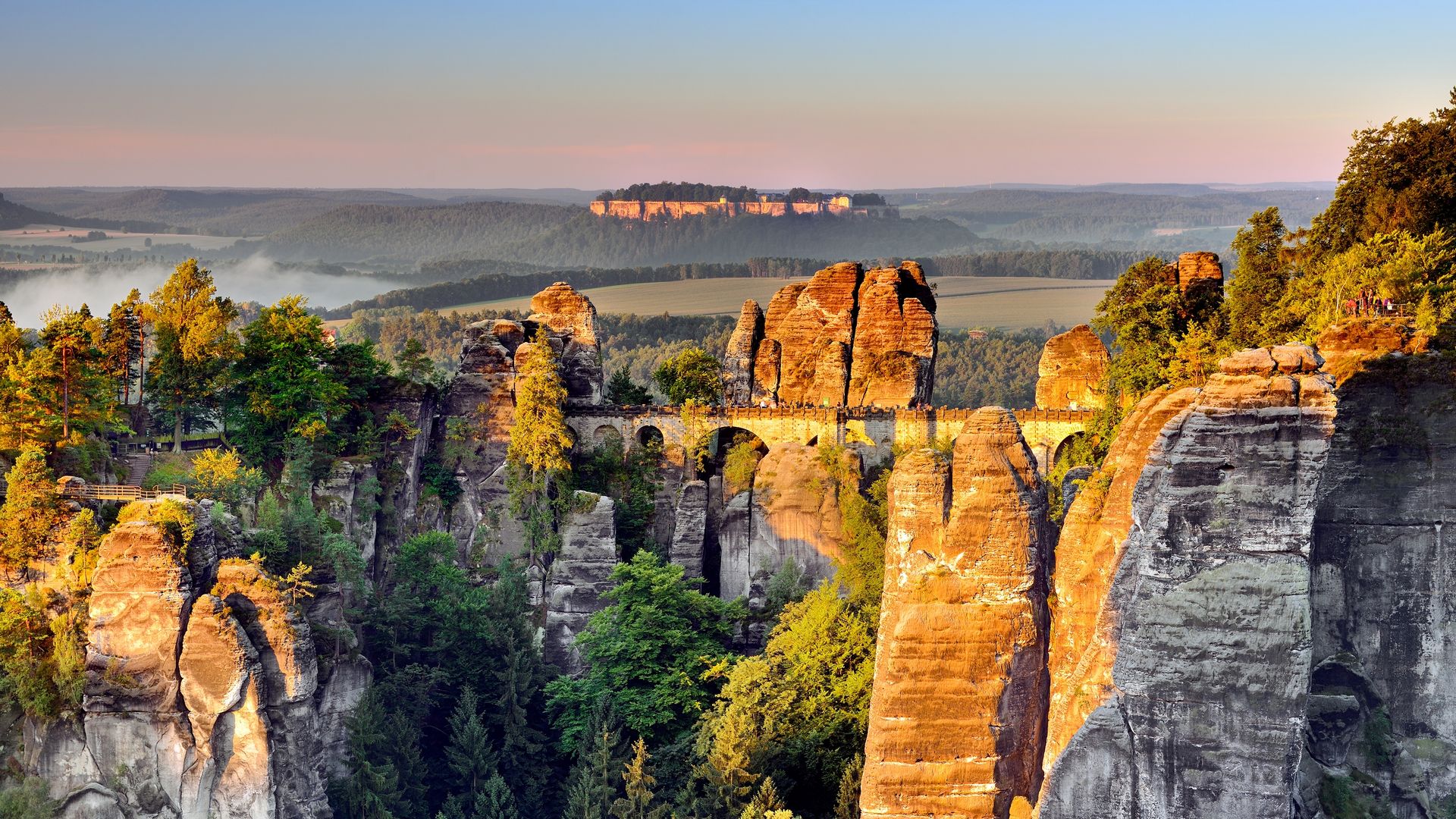 Die Sandsteinfelsen der Bastei im Nationalpark Sächsische Schweiz glänzen im Abendlicht. In der Mitte ist die berühmte Basteibrücke.