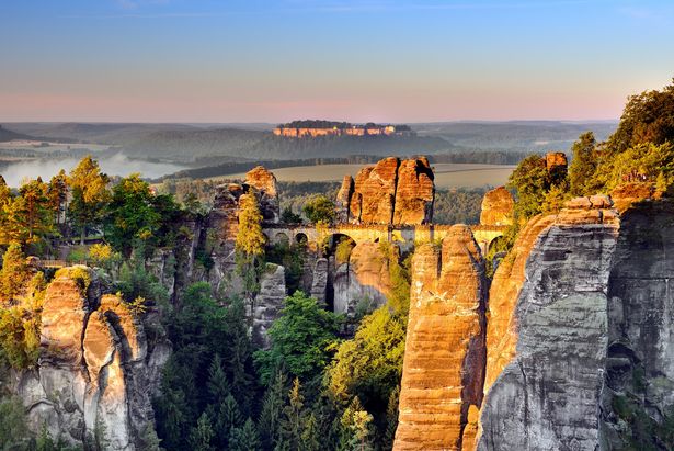 Die Sandsteinfelsen der Bastei im Nationalpark Sächsische Schweiz glänzen im Abendlicht. In der Mitte ist die berühmte Basteibrücke.