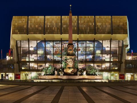 Auf dem Bild ist das Gewandhau in Leipzig in der frontalen Perspektive zu sehen. Das Konzerthaus ist innen beleuchtet. Es ist Nacht und der Himmel dunkel.