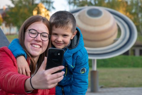 Ein Junge und ein Mädchen machen ein Selfie im Planetenpark der deutschen Raumfahrtausstellung. Hinter ihnen steht ein Planetenmodell. 